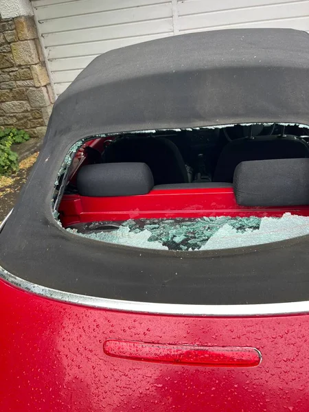 Close up of car accident smashed rear heated glass window on mohair black soft top convertible VW roof with view through hole to automobile interior and back seats with accident shattered pieces