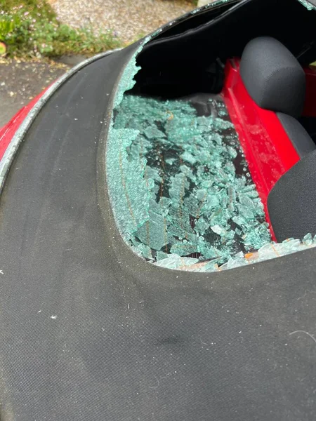 Close up of car accident smashed rear heated glass window on mohair black soft top convertible VW roof with view through hole to automobile interior and back seats with accident shattered pieces