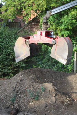 Close up  soil grab digger heavy motor machinery with digging arm bucket moving earth, lifting to clear concrete drive and dispose of rubble in re-landscaping organic garden to create level ground 