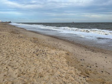 Sakin deniz suyundan uzak bir ufka sahip kumlu sahil manzarası alçak gelgitte beyaz alçak dalgalar ve yazın sonlarında okyanusun üzerinde mavi bulutlu gökyüzü.