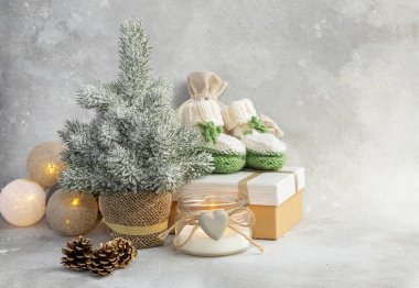 Noel arkaplanında mumlar, hediye kutuları, çelenkler ve Noel ağacı olan bir bebek için yeşil patik. Yeni yıl 2022
