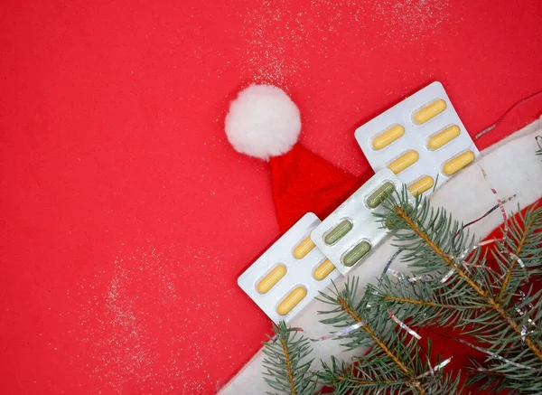 Sarı ve yeşil tıbbi kapsüllerin su toplamış hali, kırmızı arka planda Noel Baba şapkasındaki tıbbi haplar. Tıbbi Noel kavramı.