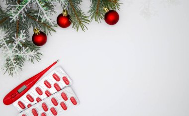 Kırmızı kapsüllü kabarcıklar, haplar ve kar taneli Noel ağacı ve üç yeni yılın kırmızı topları, fotokopi alanı olan beyaz arka planda kırmızı bir termometre. Noel Tıbbı.