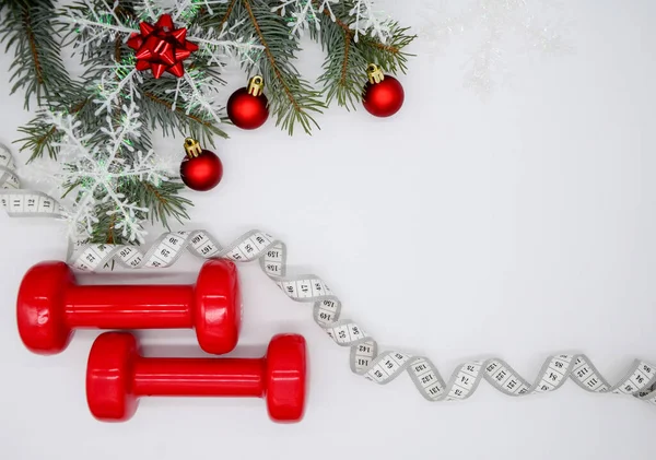 2つの赤いスポーツダンベルと雪片と赤いボールを持つクリスマスツリー コピースペースの白い背景に白い測定テープ クリスマススポーツは平等だ 健康的なライフスタイルの概念 — ストック写真
