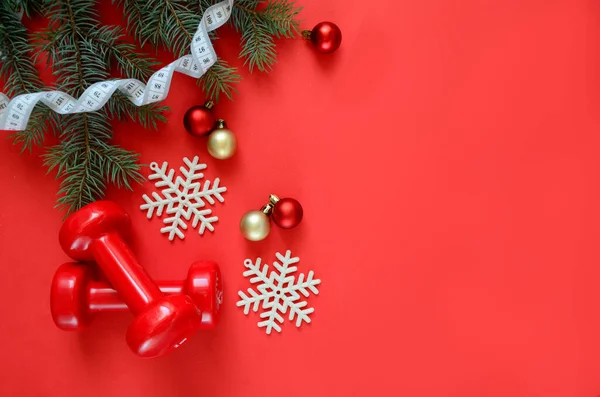 İki kırmızı spor dambılı ve kar taneleri ve kırmızı topları olan bir Noel ağacı, kırmızı arka planda fotokopi alanı olan beyaz mezura. Noel sporu. Sağlıklı yaşam tarzı kavramı.
