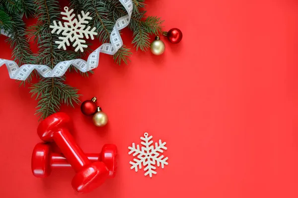 İki kırmızı spor dambılı ve kar taneleri ve kırmızı topları olan bir Noel ağacı, kırmızı arka planda fotokopi alanı olan beyaz mezura. Noel sporu. Sağlıklı yaşam tarzı kavramı.
