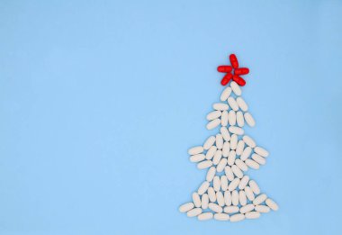 Mavi arka planda, Noel ağacı şeklinde beyaz kırmızı tıbbi haplar. Noel Tıbbı.