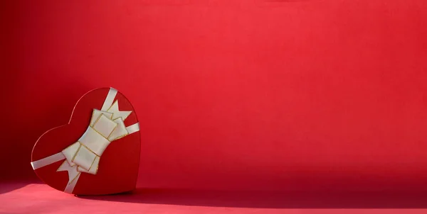 Kalp şeklinde bir hediye kutusu. Kırmızı arka planda fiyonk ve fotokopi alanı var. Sevgililer Günü hediyesi, 8 Mart, Anneler Günü, doğum günü.