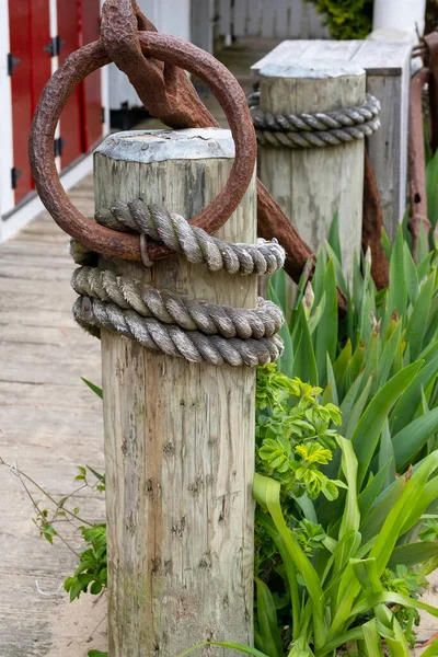 Wooden post with rusted iron rings on top and fishing rope wrapped around several poles on wooden dock on Cape Cod