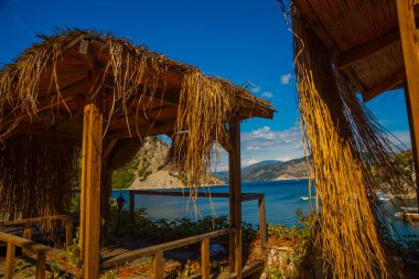 Türkiye 'nin Marmaris kenti Mugla' da güneşli bir yaz gününde, Turunc köyünün plajında palmiye ağacı çatılı ahşap çardaklar..
