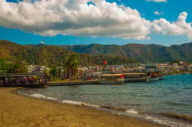 Marmaris, MUGLA, TURKEY: Türkiye 'nin Marmaris şehrinde güneşli bir günde plaj, Akdeniz ve dağların manzaralı güzel bir manzara.