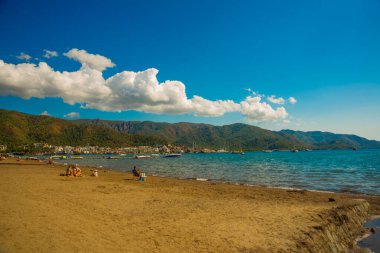 Marmaris, MUGLA, TURKEY: Türkiye 'nin Marmaris şehrinde güneşli bir günde plaj, Akdeniz ve dağların manzaralı güzel bir manzara.