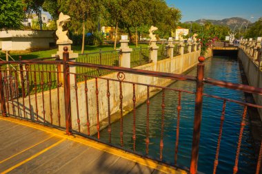 MARMARIS, MUGLA, TURKEY: Şehir manzarası kanal ve çeşme ile güneşli bir günde balık heykelleri ile modern ticaret merkezi arka planda