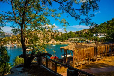 Türkiye 'nin Marmaris kenti Mugla' da güneşli bir yaz gününde, Turunc köyünün plajında palmiye ağacı çatılı ahşap çardaklar..