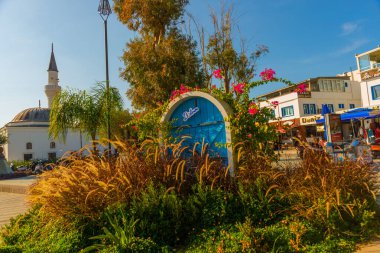 Bodrum şehrinin ismine sahip sembolik mavi kapı, güneşli bir günde Bodrum 'da mavi gökyüzünde yelken direkleri ve bougainvillea çiçeği.