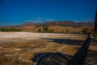 PAMUKALE, DENIZLI, TURKEY: Güneşli bir günde beyaz travertin ve dağların panoramik manzaralı güzel manzara.