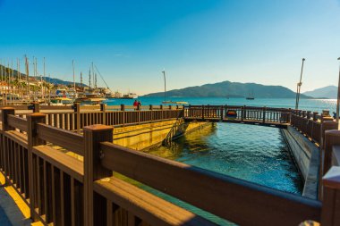 Marmaris, MUGLA, TURKEY: Güneşli bir günde Marmaris 'te deniz kenarındaki gezinti güvertesinde kanal ve ahşap köprü.
