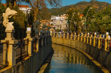 MARMARIS, MUGLA, TURKEY: Şehir manzarası kanal ve çeşme ile güneşli bir günde balık heykelleri ile modern ticaret merkezi arka planda
