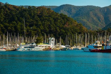 Güneşli bir günde Marmaris limanında deniz feneri ve yelkenli tekneleri.