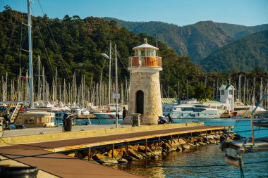 Güneşli bir günde Marmaris limanında deniz feneri ve yelkenli tekneleri.