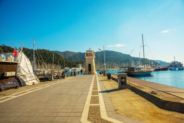 Güneşli bir günde Marmaris limanında deniz feneri ve yelkenli tekneleri.