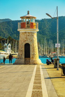 Güneşli bir günde Marmaris limanında deniz feneri ve yelkenli tekneleri.