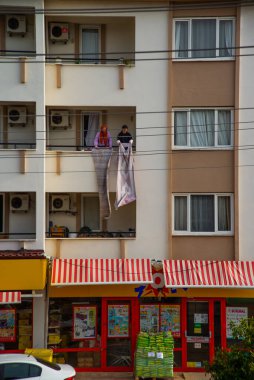 Kadınlar, evin balkonundaki halılardan süprüntüleri silkeliyor.