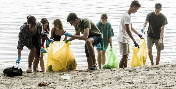a team of teenagers collect garbage on the river bank