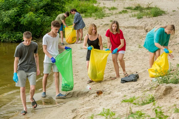 a team of teenagers collect garbage on the river bank