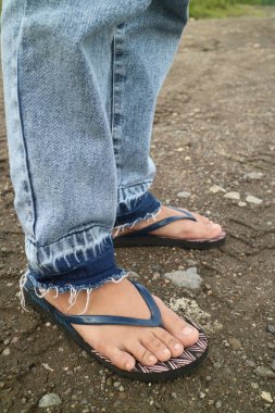 kot pantolon giyen ve parmak arası terlik giyen birinin bacakları.