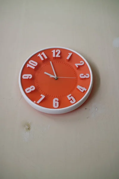 a photo of a round orange wall clock with hands indicating 10 am