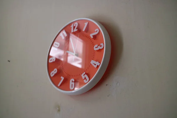 a photo of a round orange wall clock with hands indicating 10 am