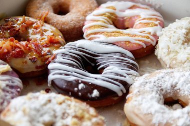 Çikolatalı, pudralı ve şekerli çöreklerle dolu bir kutuda çeşitli donutların resmi..