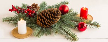 Yeni yıl afişi. Yanan mumlar, ladin dalları, kırmızı toplar, dutlu bir dal ve büyük bir sedir konisi.