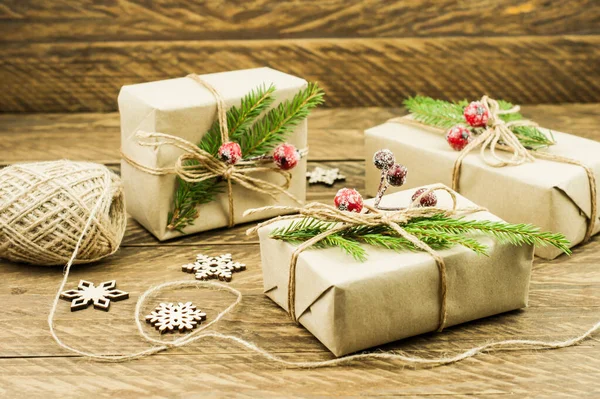 Christmas presents wrapped in craft paper with natural fir tree branches as decoration. Wooden table with wooden snowflakes and hand made New Year gifts