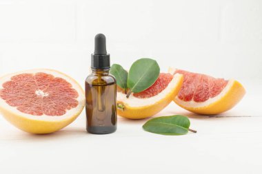 Cam şişede yüz serumu, pipet, olgun greyfurt ve beyaz ahşap arka planda meyve dilimleri.