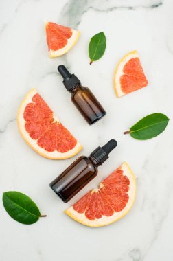 Düz plan. Greyfurt yağı ve dilimli iki şişe damlacık, mermer beyaz arka planda yapraklar. en üstteki görünüm
