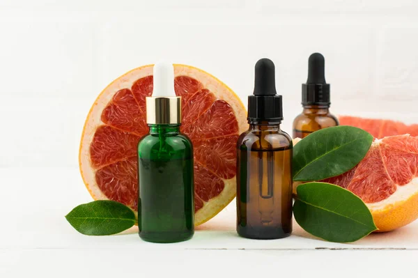 Drei Flaschen Grapefruitserum Vor Dem Hintergrund Reifer Früchte Und Blätter — Stockfoto