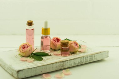 Cam şişeli beyaz ahşap puf mantar kapaklı ve pembe esanslı, gül yağlı kozmetik şişeli.