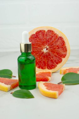 Beyaz tuğla duvar ve meyvenin arka planına karşı greyfurt esaslı yağlı yeşil camdan yapılmış bir pipetle kozmetik şişesi. Dikey.