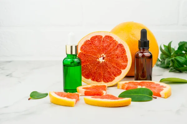 Naturkosmetik in Glasflaschen mit Pipette auf dem Hintergrund von Grapefruitfrüchten, Süßigkeiten und grünen Blättern. das Konzept der Gesichtspflege. — Stockfoto