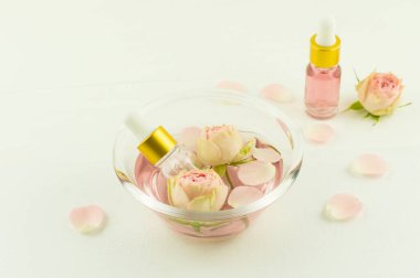 Gül suyu, çiçek ve gül yapraklarıyla dolu cam kase, zfir çiçeği yağlı kozmetik şişeler. aromaterapi, anti-stres