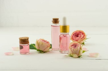 Mantar kapaklı cam şişeler ve gül suyu. Gül yağıyla kaplanmış kozmetik şişesi. Gül tomurcukları ve beyaz duvarın arka planında. Doğal Kozmetik