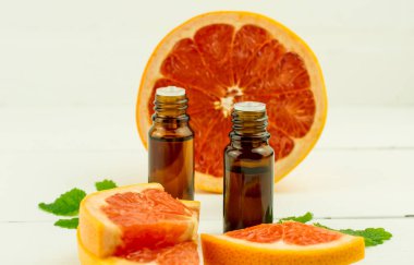 Sulu bir meyve ve beyaz ahşap bir masanın arka planında greyfurt yağı özü bulunan iki tıbbi şişe. Doğal öz bakım.