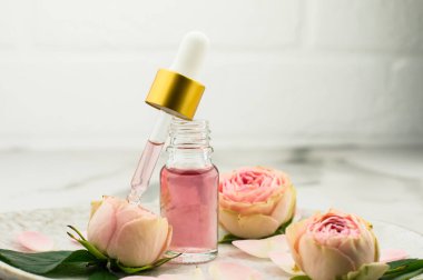Bir şişe gül yağı ve seramik tabakta yenilenme ve yüz bakımı için kozmetiklerle dolu bir pipet.