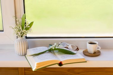 Pencerenin kenarında açık bir kitap duruyor. İçinde bir buket bahar zambağı var.