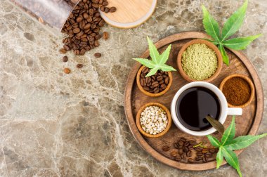 a cup of aromatic coffee with cannabis, marijuana seeds and leaves on a round wooden tray. scattered coffee beans from a glass jar. top view