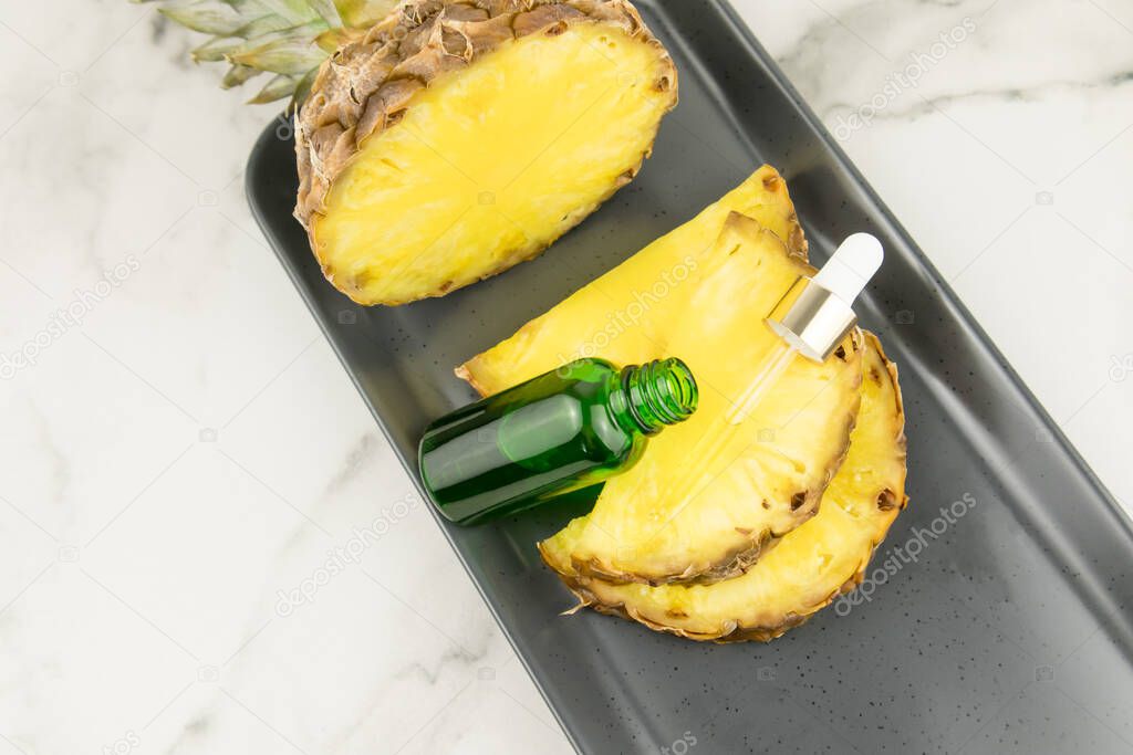 face serum with pineapple extract in a green glass bottle with a pipette filled with cosmetic products lies on pineapple slices