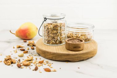 Mutfak tahtasında müsli dolu cam kavanozlar ya da avtraka yapmak için granola var. Fındık, armut, tadı güzelleşsin diye. sağlıklı beslenme