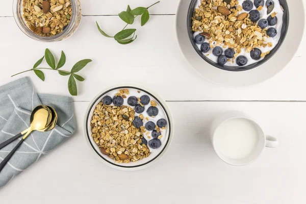 三碗烤麦片 新鲜牛奶 蓝莓和坚果的顶部视图 健康的早餐 白色木制背景 — 图库照片